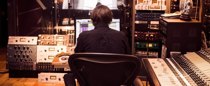 man sitting in a recording booth editing sound on a digital soundboard